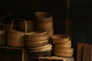 Ilustrasi: Tumpukan berbagai bentuk keranjang dan wadah anyaman bambu tertata di dalam ruangan berlatar kayu.