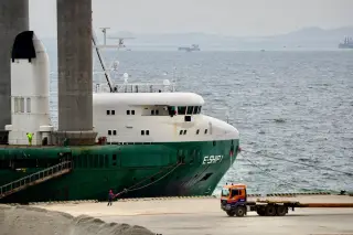 Ilustrasi: Kapal kargo hijau bersandar di dermaga pelabuhan dekat sebuah truk trailer.