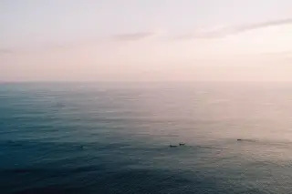 Ilustrasi: Pemandangan laut lepas yang tenang di pagi hari dengan beberapa perahu kecil di kejauhan.