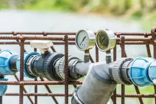 Ilustrasi: Instalasi pipa air dan pengukur tekanan pada sistem irigasi di luar ruangan.