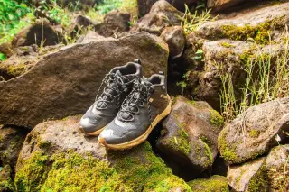 Ilustrasi: Sepasang sepatu trekking diletakkan di atas bebatuan alam yang berlumut.