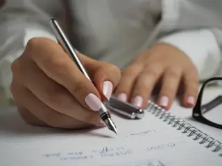 Ilustrasi: Tangan seseorang sedang menulis di buku catatan menggunakan pena bertinta.