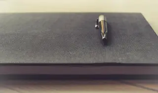 Ilustrasi: Sebuah pulpen logam berada di atas buku catatan bersampul hitam tebal.