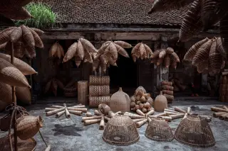 Ilustrasi: Berbagai kerajinan anyaman bambu dan perangkap ikan tradisional ditata di halaman rumah beratap genteng.