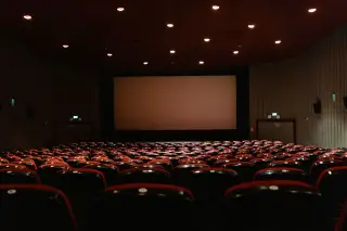 Ilustrasi: Deretan kursi merah di dalam auditorium bioskop yang kosong menghadap layar lebar.