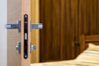 Ilustrasi: Pintu kamar kayu terbuka dengan gagang pintu logam dan latar tempat tidur.