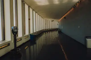 Ilustrasi: Lorong gedung melengkung yang sunyi dengan deretan jendela kaca tinggi dan lantai mengilap.