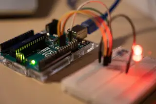 Ilustrasi: Papan mikrokontroler Arduino terhubung ke breadboard dengan kabel dan lampu LED menyala.