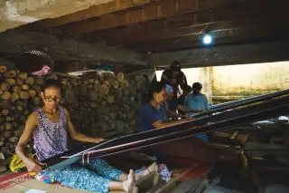 Ilustrasi: Sejumlah perempuan menenun kain secara tradisional di bawah kolong rumah panggung berkayu.