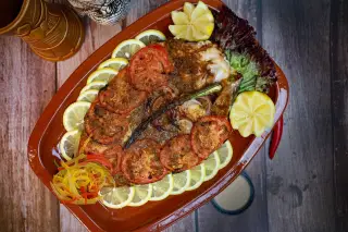 Ilustrasi: Sajian ikan bakar dengan potongan tomat dan lemon di atas piring saji oval.