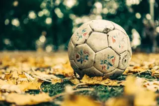 Ilustrasi: Sebuah bola sepak usang tergeletak di atas rumput berdaun gugur kuning.