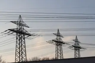 Ilustrasi: Deretan menara transmisi listrik dengan bentangan kabel di bawah langit berawan tipis.