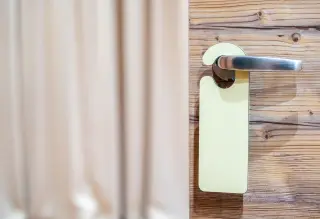 Ilustrasi: Gantungan tanda pintu terpasang pada gagang pintu kayu.