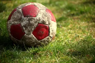 Ilustrasi: Sebuah bola sepak tua berwarna merah dan putih tergeletak di atas rumput hijau.