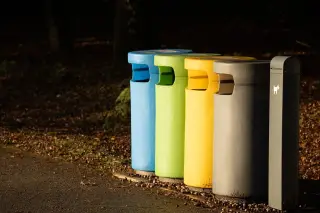 Ilustrasi: Deretan tempat sampah pilah warna-warni di tepi jalan luar ruangan.