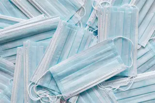 Ilustrasi: Tumpukan masker medis sekali pakai berwarna biru muda yang tertata acak.
