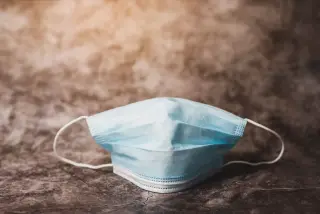 Ilustrasi: Sebuah masker medis sekali pakai berwarna biru diletakkan di atas permukaan bertekstur.