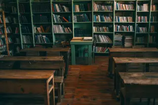 Ilustrasi: Deretan bangku kayu tua di dalam ruangan kelas dengan rak buku besar di dinding.