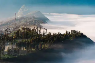 Ilustrasi: Pemandangan perbukitan hijau berselimut kabut tebal dengan deretan pepohonan dan menara pemancar.