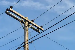 Ilustrasi: Tiang listrik kayu dengan kabel transmisi berlatar langit biru cerah.