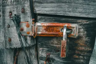 Ilustrasi: Gembok besi berkarat terpasang pada grendel pintu kayu tua.