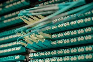 Ilustrasi: Kabel serat optik biru terhubung ke panel soket pada rak peladen data.