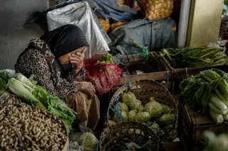 Ilustrasi: Seorang wanita lansia duduk di pasar tradisional dikelilingi sayur-mayur dan kacang dalam keranjang.