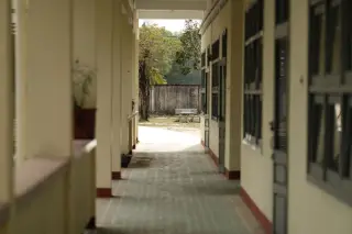 Ilustrasi: Lorong panjang sebuah bangunan kosong dengan tiang-tiang dan pemandangan ke luar.