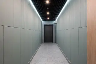Ilustrasi: Lorong modern yang sepi dengan pencahayaan lampu langit-langit menuju sebuah pintu tertutup di ujungnya.