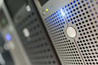 Ilustrasi: Detail rak server komputer dengan lampu indikator menyala di pusat data.