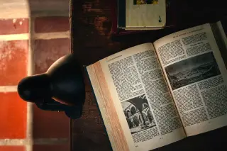 Ilustrasi: Buku tebal terbuka di atas meja kayu di sebelah lampu meja kecil bercahaya lembut.
