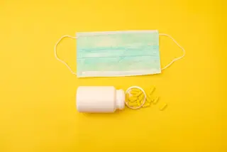 Ilustrasi: Masker medis dan botol berisi kapsul obat kuning di atas latar belakang kuning cerah.