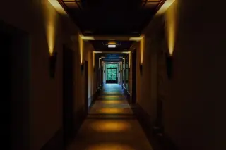 Ilustrasi: Lorong panjang yang sepi dengan pencahayaan lampu dinding temaram menuju pintu kaca di ujung.