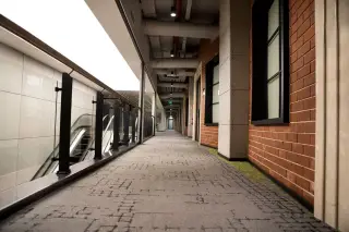 Ilustrasi: Lorong bangunan modern yang sepi dan bersih dengan karpet bermotif serta eskalator di sisi kiri.