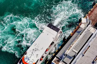 Ilustrasi: Pemandangan dari atas sebuah kapal feri yang merapat di dermaga dengan buih air laut biru kehijauan.