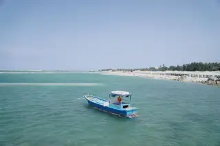 Ilustrasi: Sebuah perahu kayu berwarna biru tertambat di perairan dangkal dekat pantai berpasir.