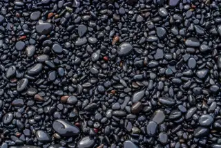 Ilustrasi: Hamparan batu kerikil hitam yang basah dan licin di tepi pantai.