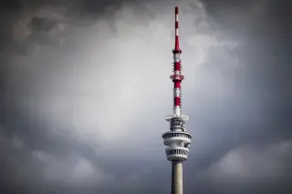 Ilustrasi: Menara pemancar telekomunikasi tinggi bergaris merah putih dengan latar belakang langit berawan mendung.